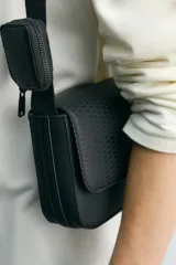 Bandolera de hombre con acabado engomado en color negro, con solapa frontal texturizada y cierre de botón a presión. Cuenta con correa de hombro ajustable e incluye un pequeño monedero desmontable con cierre.
