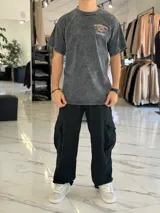 Remera oversize gris con efecto gastado, de manga corta, con estampa en la espalda de estilo surf con la inscripción "Mushkana Surf House".
