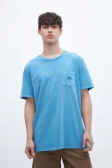 Remera celeste de algodón con bolsillo en el pecho, teñida en prenda. Tiene una etiqueta en el bolsillo y un estampado en la espalda.