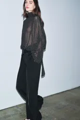 Blusa negra con estampado de lunares blancos, cuello redondo con lazadas y manga larga con puños ajustados. El bajo es ajustable con cordones.