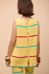 Top sin mangas de punto acanalado color amarillo, con cuello redondo y terminaciones festoneadas en piquitos. Presenta botones decorativos en forma de florcitas en la parte delantera.