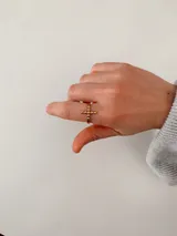 Anillo ajustable de acero quirúrgico en color dorado, con un dije central en forma de cruz compuesto por pequeñas esferas.