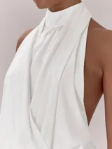 Top blanco con diseño halter, cuello alto y espalda descubierta. Presenta un frente cruzado con pliegues, bajo elástico y lazo de ajuste en la espalda.