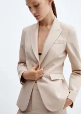 Blazer entallado de color beige con solapas de muesca, hombros estructurados y cierre frontal de un botón. Presenta bolsillos de ribete delanteros, pinzas de entalle y abertura posterior.