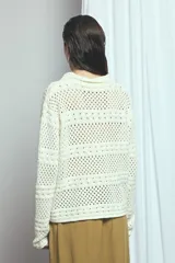Cardigan de punto calado color marfil, con cuello solapa, cierre frontal de botones oscuros y bolsillos frontales.