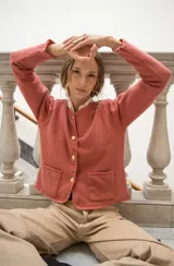 Cardigan de punto color beige con cuello redondo, cierre frontal con botones dorados, bolsillos frontales y terminaciones en crochet. Presenta hombreras internas y diseño de corte recto.