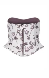 Corset strapless con cierre frontal metálico, confeccionado en tela con estampado de rosas en tonos violeta sobre fondo claro. Presenta un diseño estructurado con volumen en la zona de la cadera.