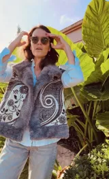 Chaleco reversible con un lado de piel sintética gris y el otro lado de tela bordada con diseño floral y espiral en tonos blanco y negro. Presenta un diseño sin mangas y corte recto.