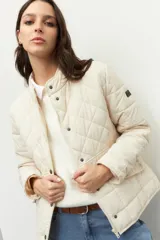 Campera capitoneada de cuello alto, con cierre frontal y solapa con botones metálicos. Presenta diseño acolchado con costuras en forma de rombos y bolsillos delanteros con solapa.