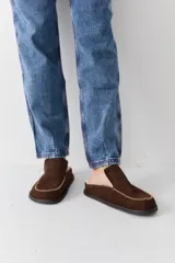 Zueco de cuero color marrón oscuro, con costuras decorativas en hilo rojo en el empeine y suela plana de goma.