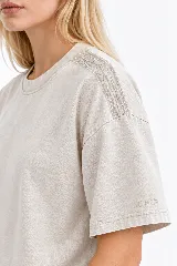 Remera oversize de algodón con acabado stonewash, color gris azulado, manga corta y cuello redondo. Cuenta con apliques bordados a mano en forma de hojas con canutillos plateados sobre los hombros.