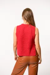 Chaleco de punto texturizado color rojo, con cuello redondo y diseño sin mangas. Presenta un corte recto con aberturas laterales y un largo asimétrico, siendo más corto en la parte frontal.
