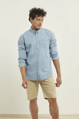 Camisa de hombre de denim azul, manga larga, con cuello buttondown y un bolsillo de parche en el pecho izquierdo.