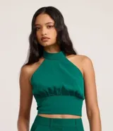 Top cropped de crepé color verde esmeralda, con escote halter y cuello alto. Presenta un canesú fruncido en la cintura que ajusta la prenda al cuerpo.