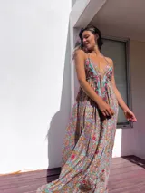 Vestido largo de estilo boho, con estampado tipo paisley en tonos tierra, turquesa y rosa. Presenta un escote profundo con tirantes finos y detalles de bordados florales en color rojo y verde a lo largo del frente.