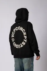 Buzo canguro oversize de frisa de algodón premium en color azul grisáceo. Presenta un diseño con recortes frontales, bolsillo tipo canguro y un pequeño logo circular estampado en el pecho. Cuenta con puños y ruedo acanalados.