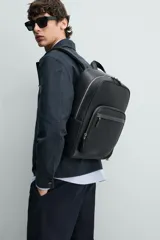 Mochila de diseño minimalista en color negro con acabado grabado. Cuenta con compartimento principal con cierre, bolsillo frontal con cierre, asa de mano superior y correas de hombro ajustables y acolchadas. Incluye espacio interior para dispositivos electrónicos y bolsillo de seguridad trasero.