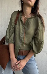 Camisa verde de tejido liviano, con cuello romántico con volados, mangas abullonadas tres cuartos con puños fruncidos y cierre frontal con botones.