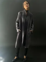 Tapado largo gris de lana merino con bolsillos laterales y corte particular en los hombros.