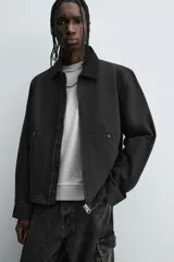 Cazadora de algodón color negro lavado, de corte relajado (relaxed fit), con cuello solapa a contraste, cierre frontal de cremallera, bolsillos canguro en la cadera y puños con botón a presión.