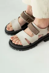 Sandalias de cuero marrón con diseño de tiras anchas y ajuste mediante velcro. Presentan una plantilla acolchada color tostado con detalles en rojo y una suela de goma negra con plataforma dentada.