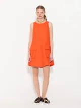 Vestido corto color naranja, sin mangas, con cuello redondo y dos bolsillos frontales con botón.