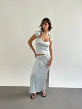 Conjunto de dos piezas compuesto por un top de cuello redondo con detalle de lazo y mangas cortas, y una falda larga con tajos laterales. Ambas prendas presentan un diseño estampado con motivos botánicos.