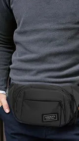 Riñonera negra de tafeta con tres bolsillos con cierre, uno frontal y correa de galón ajustable.