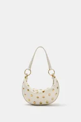 Bolso de hombro de diseño saca multiposición color blanco, decorado con tachas metálicas doradas y aros metálicos que conectan el cuerpo con la manija. Cuenta con cierre de cremallera metálica y bolsillo interior.