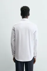 Camisa blanca de manga larga con cuello italiano y puños abotonados, confeccionada en tejido de algodón.