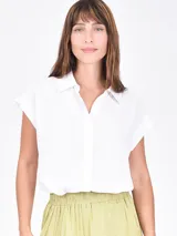 Camisa blanca de manga corta, con cuello camisero y botones frontales. Presenta un corte recto y holgado.