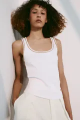 Musculosa de algodón color blanco con cuello redondo amplio y sisas. Cuenta con detalles de ribetes dorados brillantes en el escote, tirantes y costuras laterales.