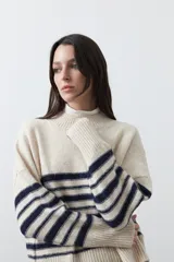 Polera de tejido de punto con diseño a rayas horizontales en color azul marino sobre base beige. Presenta cuello alto, mangas largas con puños acanalados y una silueta relajada.