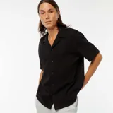 Camisa negra de manga corta con cuello solapa y cierre abotonado.