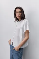 Camisa negra de manga corta, con cuello mao y cierre frontal de botones, de silueta amplia y tejido liviano con textura sutil.