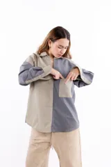 Camisa oversize bicolor con diseño de paneles en tonos beige y gris con rayas verticales. Presenta cuello clásico, bolsillo frontal y cierre frontal con botones, confeccionada en tejido de lana con caída fluida.