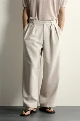 Pantalón relaxed fit de color blanco off-white, confeccionado en tejido con lino. Cuenta con pliegues frontales en la cintura, bolsillos delanteros y cierre frontal con cremallera y botón.