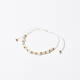 Pulsera con hilo blanco ajustable y cuentas de piedra blanca y dorada.