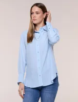 Camisa de calce relajado color celeste, confeccionada en tejido de textura suave y fluida. Presenta cuello camisero y abotonadura frontal, mangas largas con puño ancho y ruedo curvo.