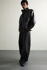 Cazadora biker relaxed fit confeccionada en tejido efecto piel, color negro. Cuenta con cuello subido, manga larga con puño ajustable y bajo elástico. Incluye bolsillos de vivo en la cadera y cierre frontal con cremallera oculta bajo una solapa diagonal con botones a presión.