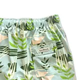 Short de baño con estampado botánico y abstracto en tonos verdes y crema sobre fondo celeste. Cuenta con cintura elástica con cordón ajustable, dos bolsillos laterales, un bolsillo trasero y malla interior hipoalergénica.