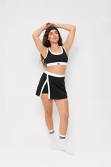 Conjunto deportivo compuesto por un top y una pollera short. El top es de estilo deportivo con cuello redondo y ribetes blancos en contraste. La pollera short cuenta con un diseño de tajo lateral con borde blanco y cintura elástica a juego.