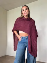 Ruana tejida de algodón con hilo lurex en punto jersey, color azul, con diseño amplio y detalle de etiqueta de cuerina en la parte posterior.