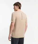 Remera deportiva de hombre con tecnología dry fit, cuello redondo y manga corta. Presenta un diseño liso en color beige con una pequeña etiqueta decorativa en el dobladillo.