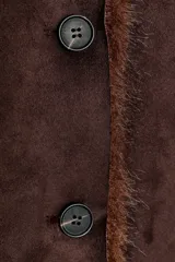 Cazadora reversible de corte recto, con cuello de solapa, manga larga y cierre frontal con botones. Presenta un exterior efecto ante y un interior con acabado de pelo sintético, incluyendo detalles de pelo en los bordes.