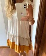 Vestido corto de lino color blanco con falda escalonada en lila y ocre. Tiene escote cuadrado, mangas cortas con volados y corte holgado.