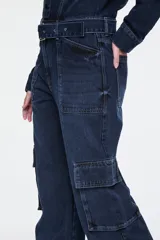 Enterito largo confeccionado en denim azul, con cuello camisero, cierre frontal con botones, mangas largas, cinturón incorporado con hebilla metálica, bolsillos aplicados en el pecho y bolsillos estilo cargo en los laterales de las piernas.