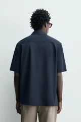 Camisa azul marino de corte regular fit confeccionada en tejido fluido de algodón y lino, con cuello solapa, manga corta, bolsillo aplicado en el pecho y cierre frontal con botones.
