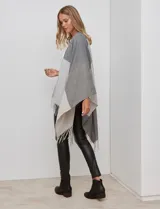 Ruana tejida con diseño colorblock en tonos de gris y beige, con flecos en el borde inferior.