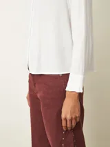 Camisa de manga larga color blanco, con cuello alto tipo mao con detalle de volados y cierre frontal de botones.